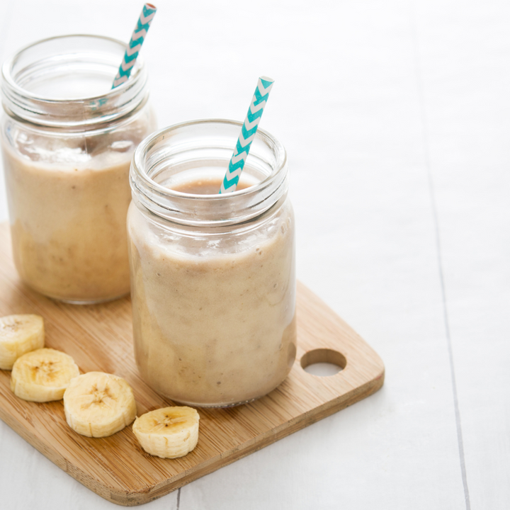 Two mason jars of banana smoothies with slices of bananas on wooden plate