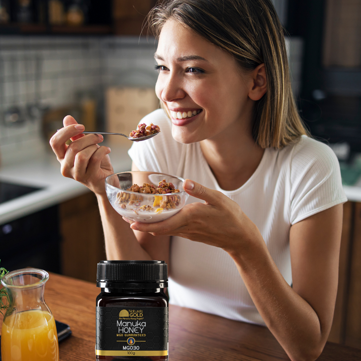A woman eating breakfast with a bottle of orange and a bottle of Nature's Gold manuka honey MGO30