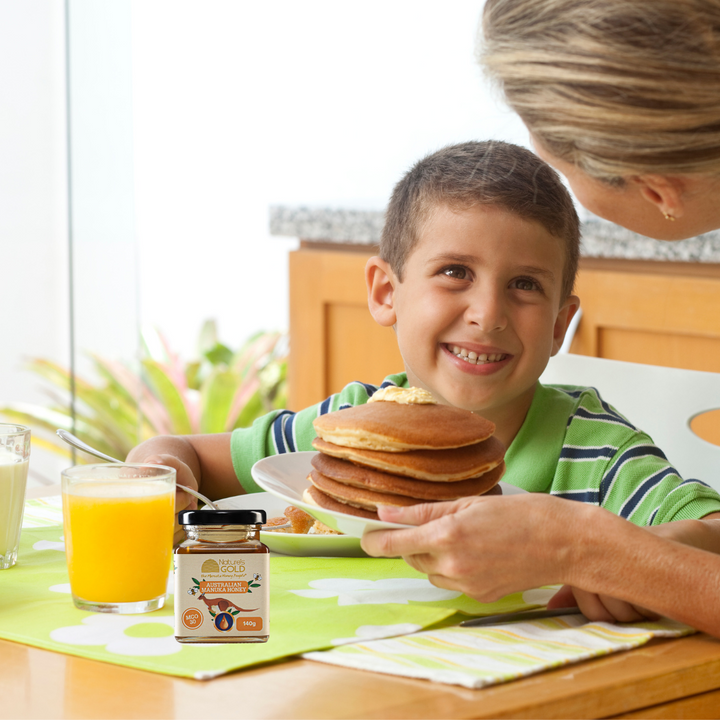 A child being served a plate of pancakes with a bottle of manuka honey kangaroo label