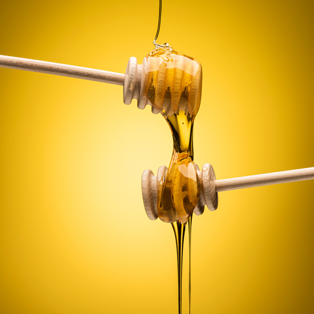 Honey dripping from one honey spoon to another on yellow background