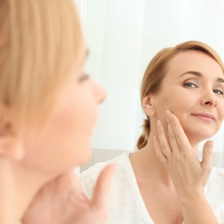 A middle-age lady looking at her skin in the mirror 